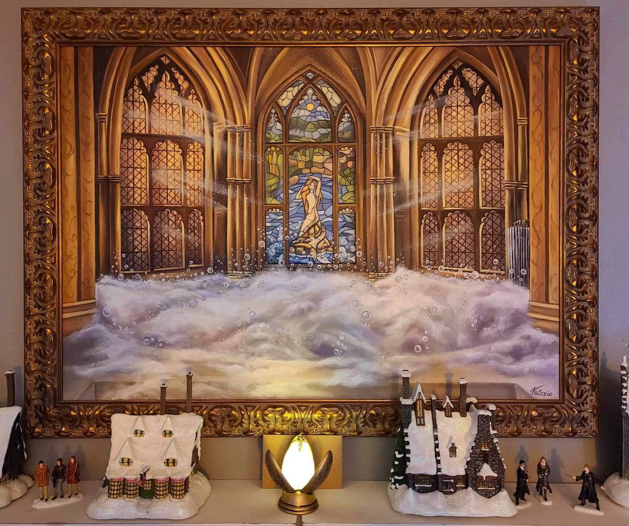 A gold-framed painting of a Gothic bathing hall, a mermaid stained-glass window and white foam, displayed above a miniature village.