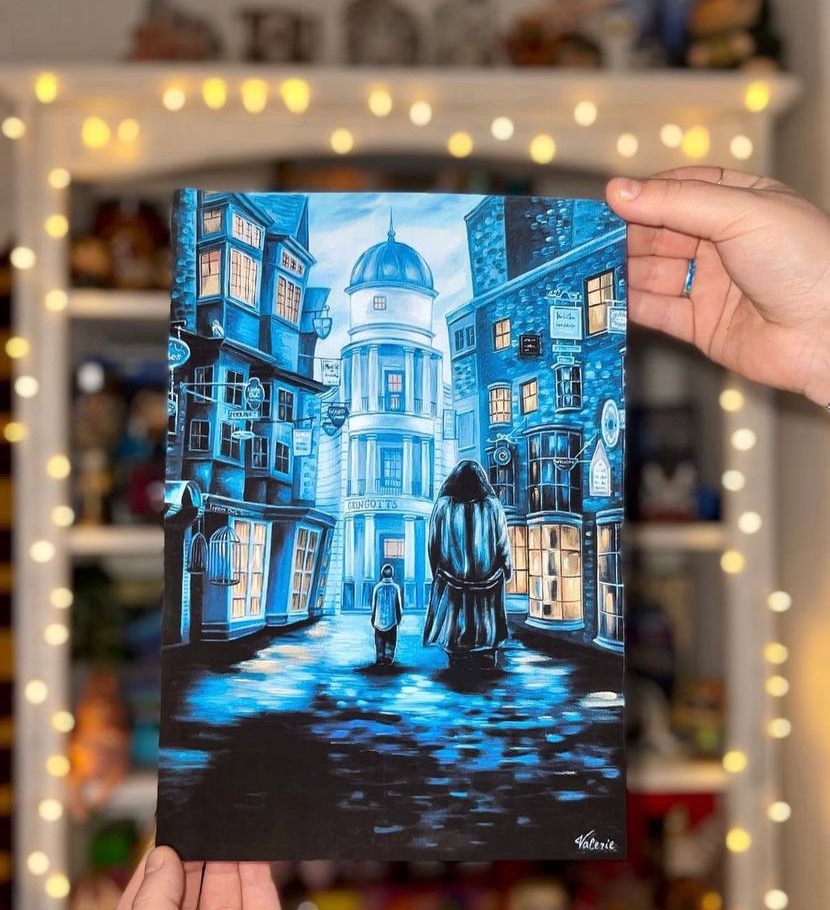 A collector holds a blue-toned print of two figures walking through a magical street, against shelves lit with warm fairy lights.