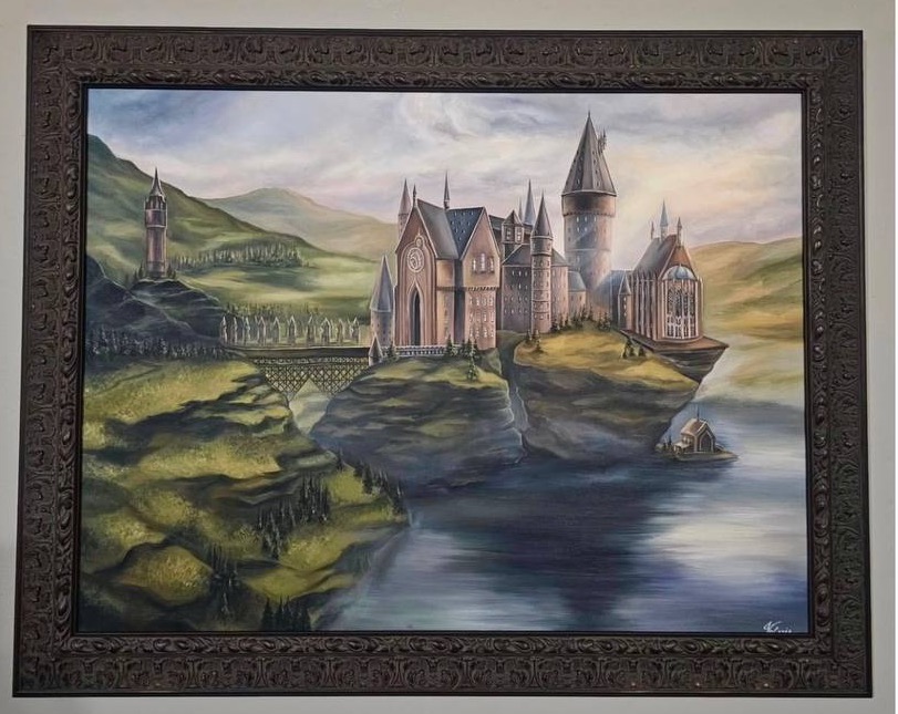 A framed painting of a castle overlooking a lake and green hills, hanging on the collector’s wall.